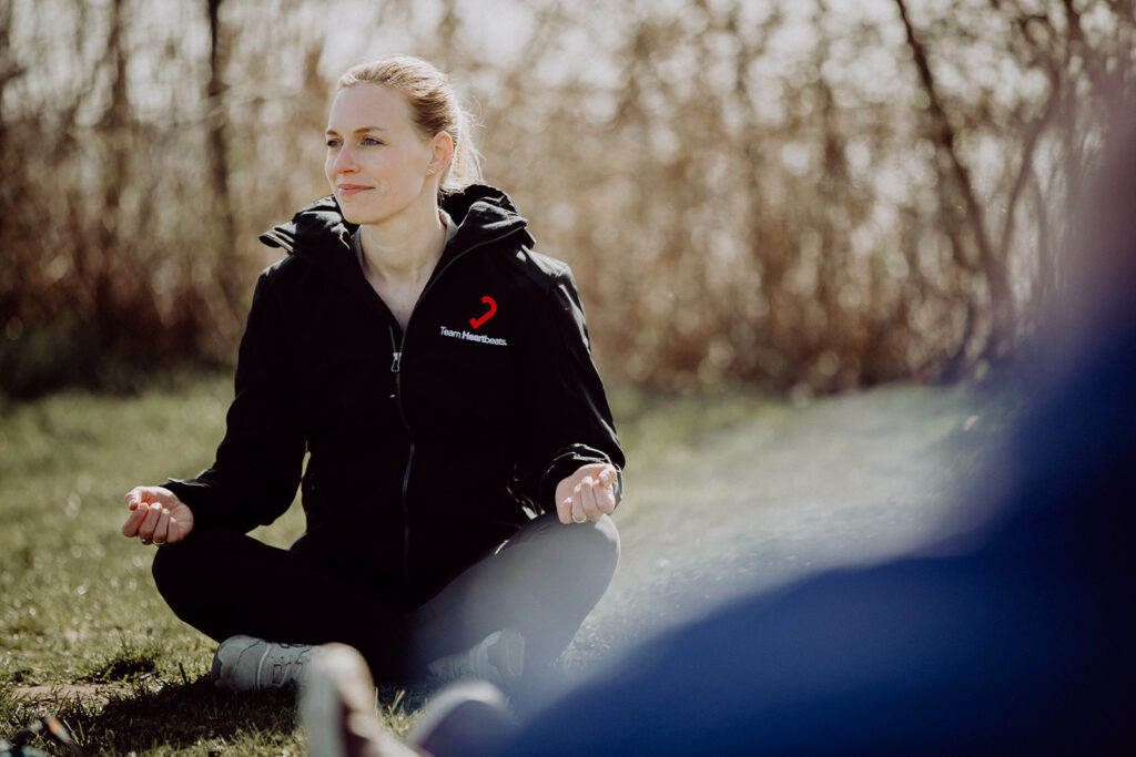 A woman in a black jacket practicing team development by meditating in the grass, cultivating resilience and improving her team training skills.