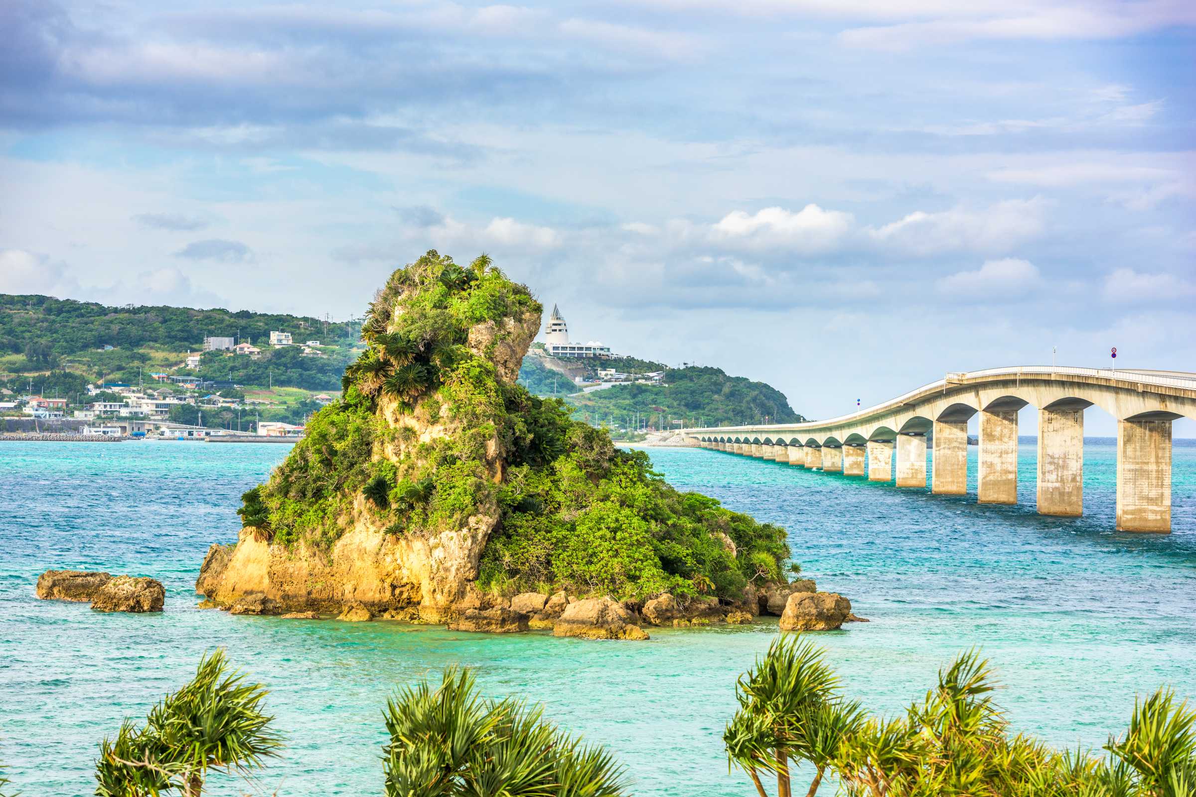 Een schilderachtig uitzicht op het eiland Kouri in Okinawa, Japan, met een weelderig groen eilandje dat met het hoofdeiland is verbonden door een lange brug over turquoise water, waar bezoekers kunnen zitten en genieten