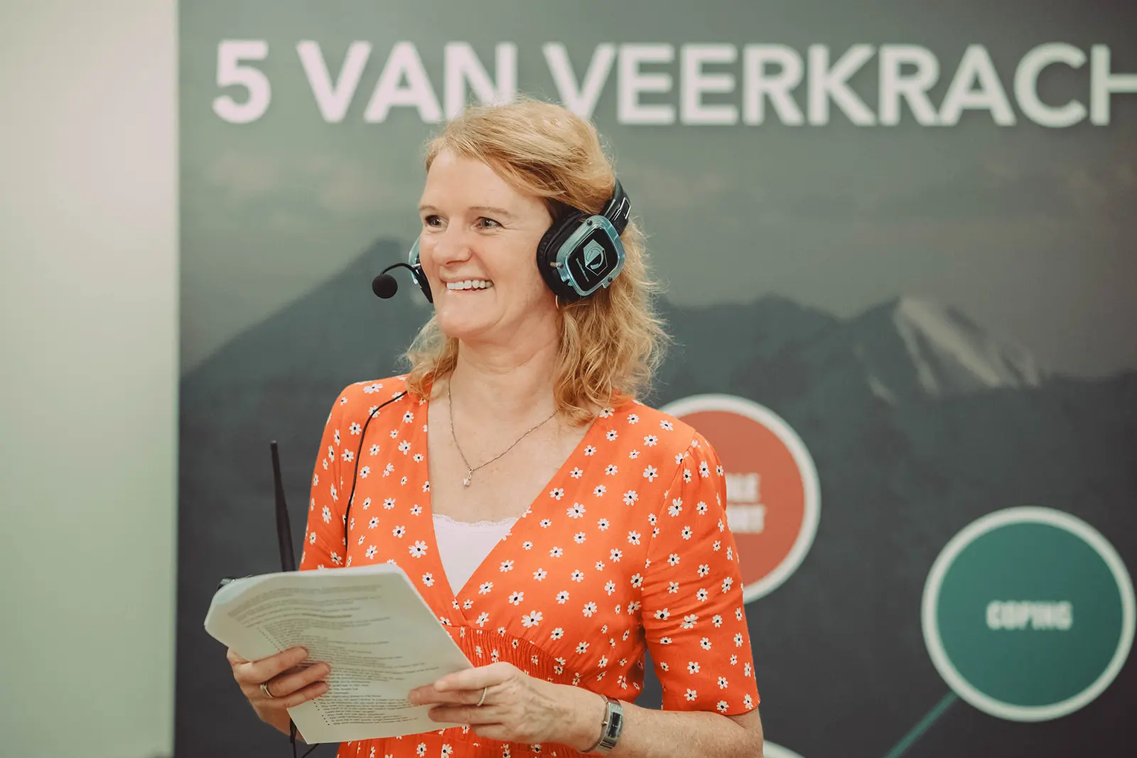 A smiling woman in headphones poses resiliently in front of a sign.